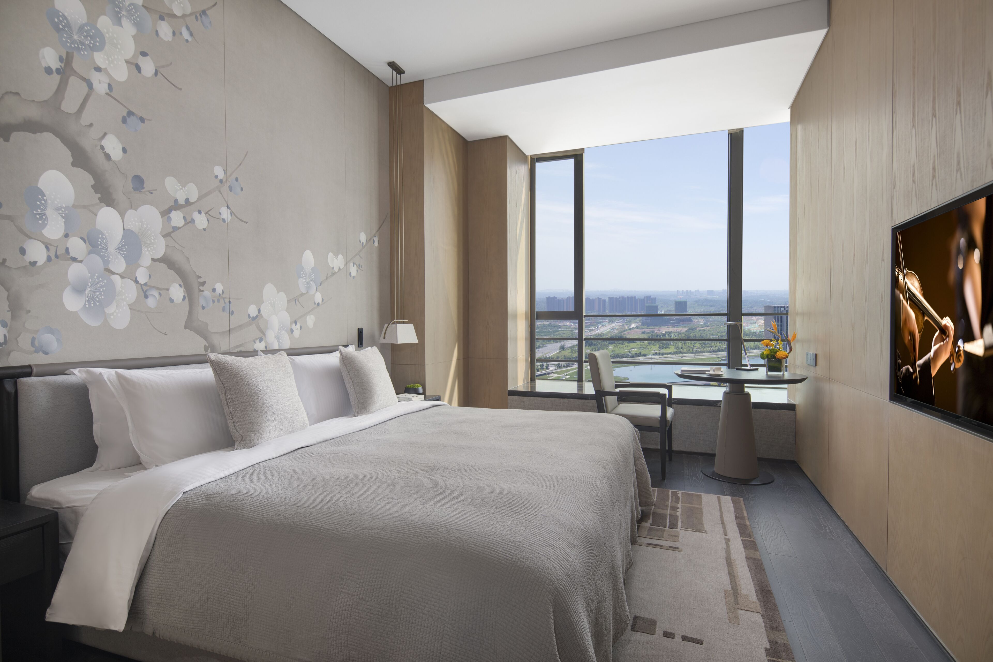 A modern hotel room with a large bed, a desk with a chair, and a TV.