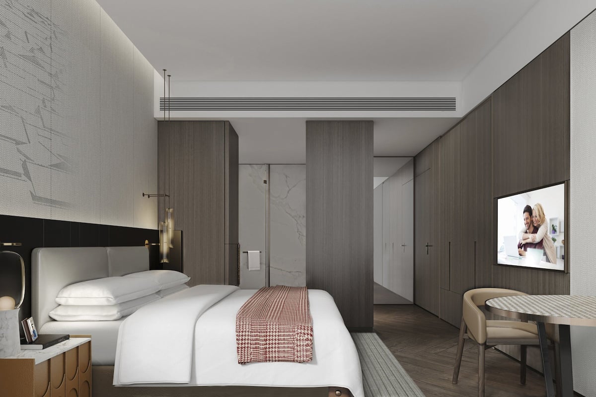 A modern hotel room with a large bed, a bedside table, a chair, and a TV screen.