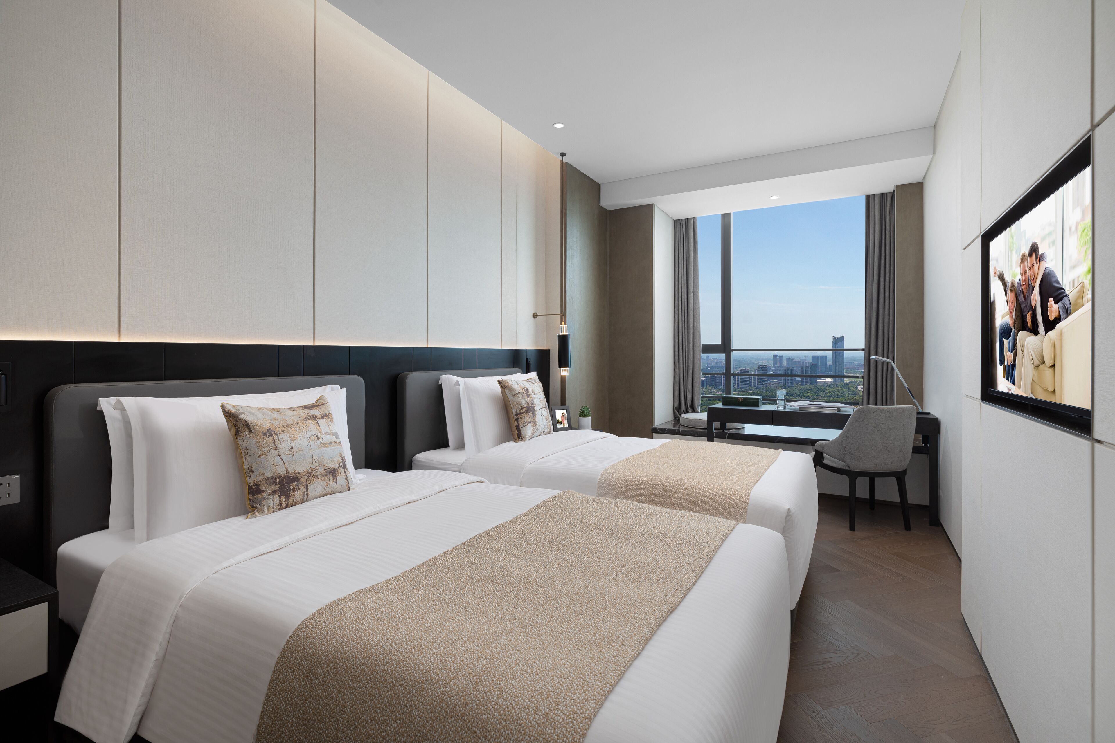Ein modernes Hotelzimmer mit zwei Betten, einem Schreibtisch und einem großen Fenster mit Blick auf die Stadt.