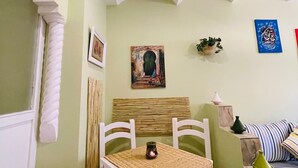 A dining area with a table, chairs, a woven table runner, a painting on the wall, and a sofa with striped cushions. - Charming Getaway in Casablanca Maroc, Cozy Home with Thoughtful Amenities (Casablanca)