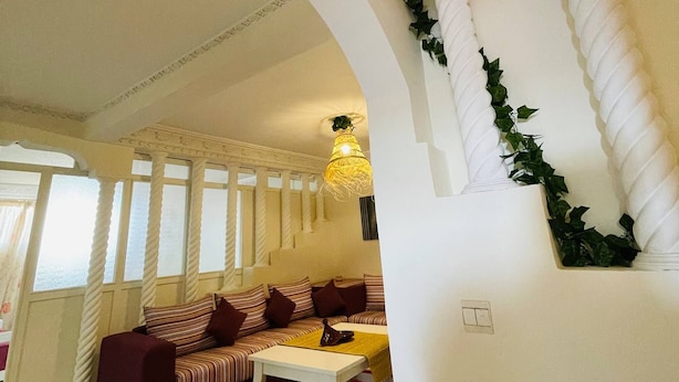 A room with a sofa, a small table, a hanging light fixture, and a window with curtains. - Coquet Appartement À Casablanca (Casablanca)