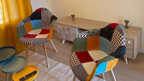 Un salon moderne avec deux fauteuils colorés, une petite table en bois, un téléviseur fixé au mur et un rideau jaune.
