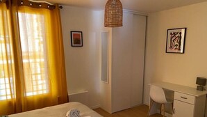 Une chambre d’hôtel comprenant un lit, un bureau, une chaise, une armoire et un luminaire suspendu.