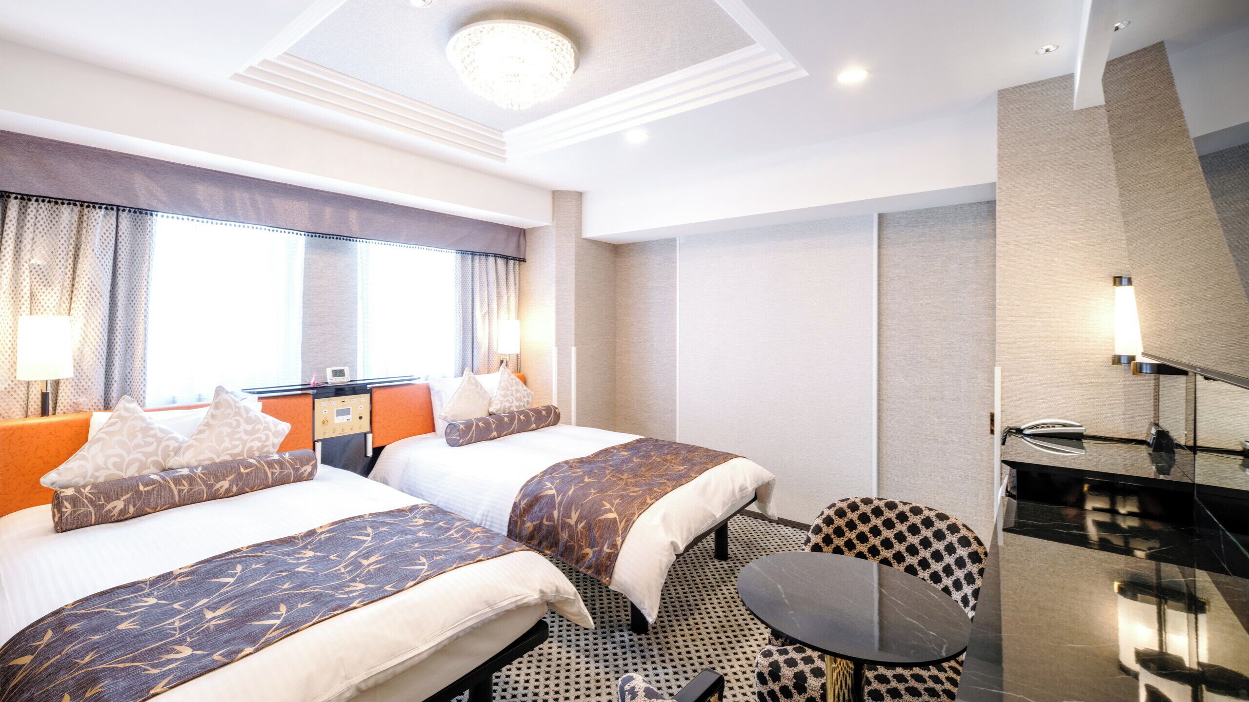 Ein Hotelzimmer mit zwei Betten, einem kleinen runden Tisch, einem Sessel, einem Schreibtisch mit Lampe und einem großen Spiegel.