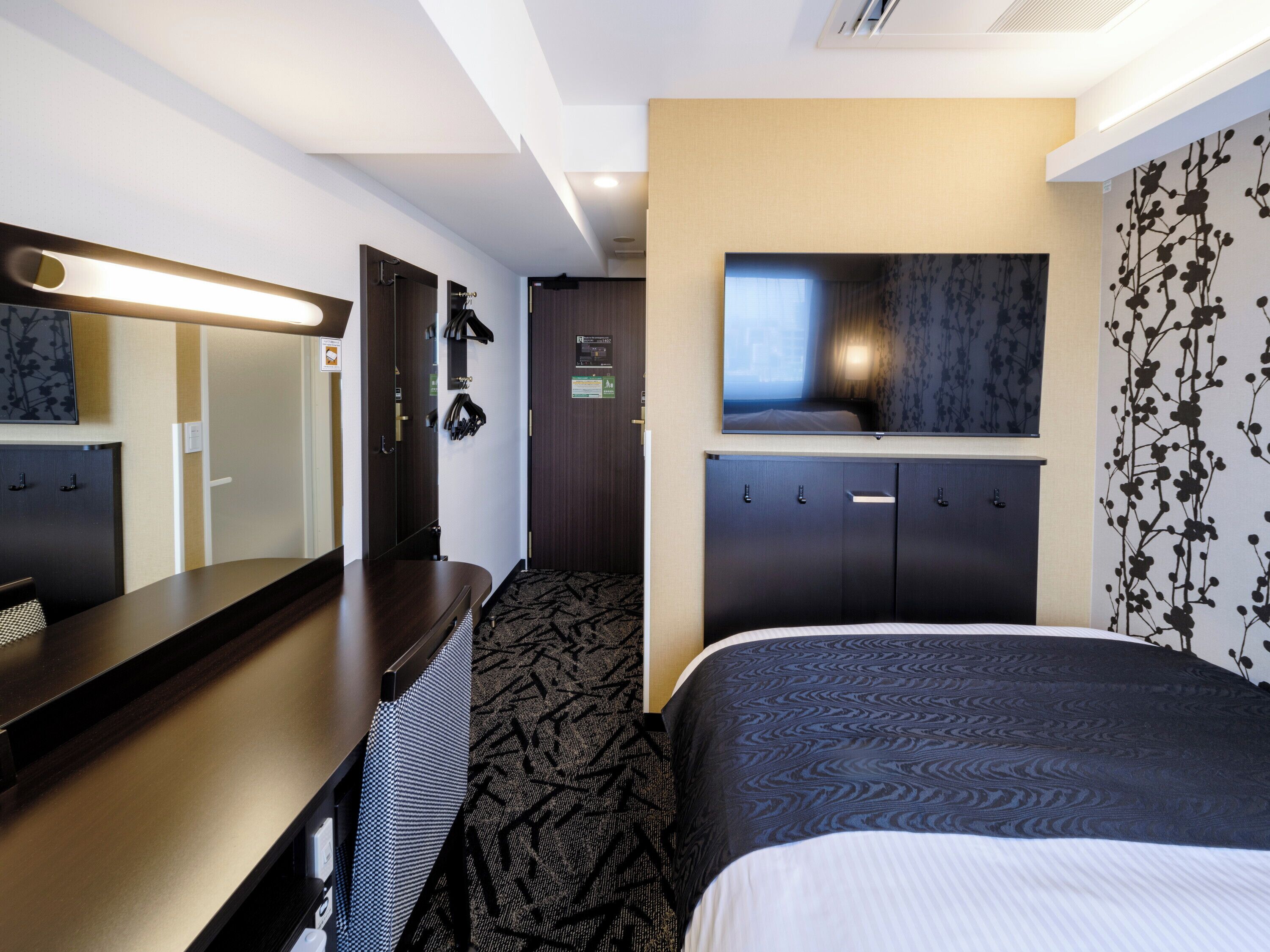 Ein Hotelzimmer mit Bett, Schreibtisch, Spiegel, Fernseher und Kleiderschrank.