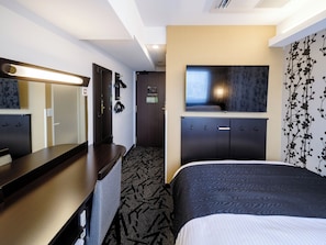 Quarto de hotel com cama, escrivaninha, espelho, televisão e guarda-roupa.