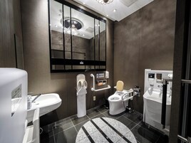Une salle de bain moderne avec un grand miroir, des toilettes dotées d’un abattant surélevé, un bidet et un lavabo.