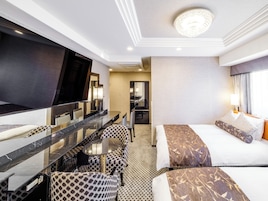 Quarto de hotel com cama grande, mesa de jantar com cadeiras, pequena cozinha e um espelho grande.