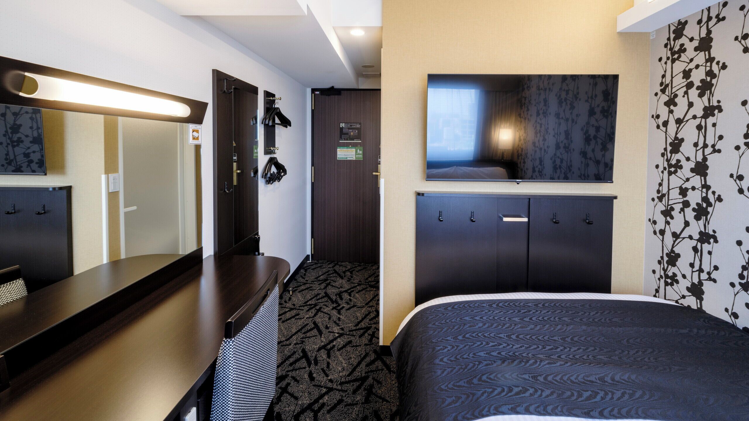 Ein Hotelzimmer mit Bett, Schreibtisch, Spiegel, Kleiderschrank und Duschbereich.