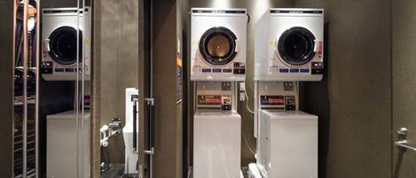 A hotel laundry room with three stacked washing machines and a dryer.