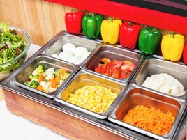 Un bufé con diversas opciones de comida, incluyendo verduras, maíz y zanahorias ralladas.