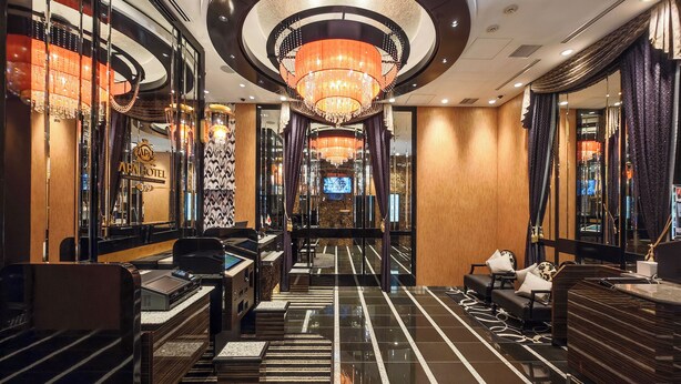Eine Hotelhalle im modernen Stil, mit einem zentralen Kronleuchter, einer Rezeption und einer Sitzecke.