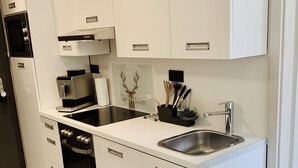 A modern kitchen with white cabinetry, stainless steel appliances, and a built-in oven. - Ferienwohnung "ME 7" (Mettmann)