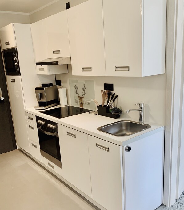 A modern kitchen with white cabinetry, stainless steel appliances, and a built-in oven.