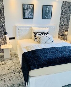 A neatly arranged bedroom with a bed, pillows, a nightstand, and wall art.