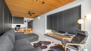 A modern living room with a grey sofa, leather armchair, and a wooden ceiling. - Kings Edge Unit 4 Kings Beach QLD (Kings Beach)