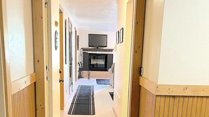 Ein Korridor führt zu einem Wohnbereich mit Kamin, Fernseher und Esstisch.