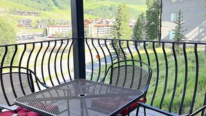 Ein Balkon mit einem Metalltisch und Stühlen, roten Kissen sowie Blick auf einen Berg und Gebäude im Hintergrund.