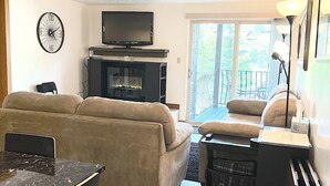 Ein Wohnzimmer mit einer Couch, einem Fernseher, einem Kamin und einem Essbereich mit Tisch und Stühlen.