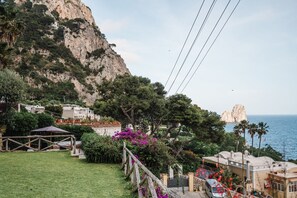 A coastal property with a view of the sea, a rocky cliff, and a garden area with a wooden pergola. - Villa Michika by Elite Villas (Capri)