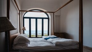 A bedroom with a bed, a lamp, and a view of the sea through a window. - Villa Michika by Elite Villas (Capri)