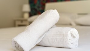 Two rolled white towels on a bed in a hotel room.