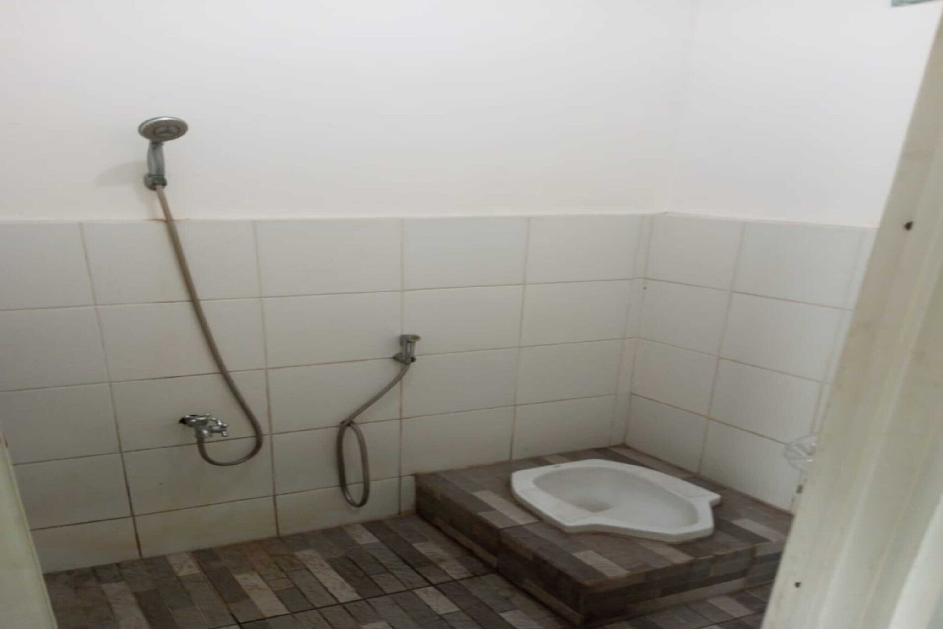 Een kleine betegelde badkamer met een douche, toilet en een trede naar het toilet.