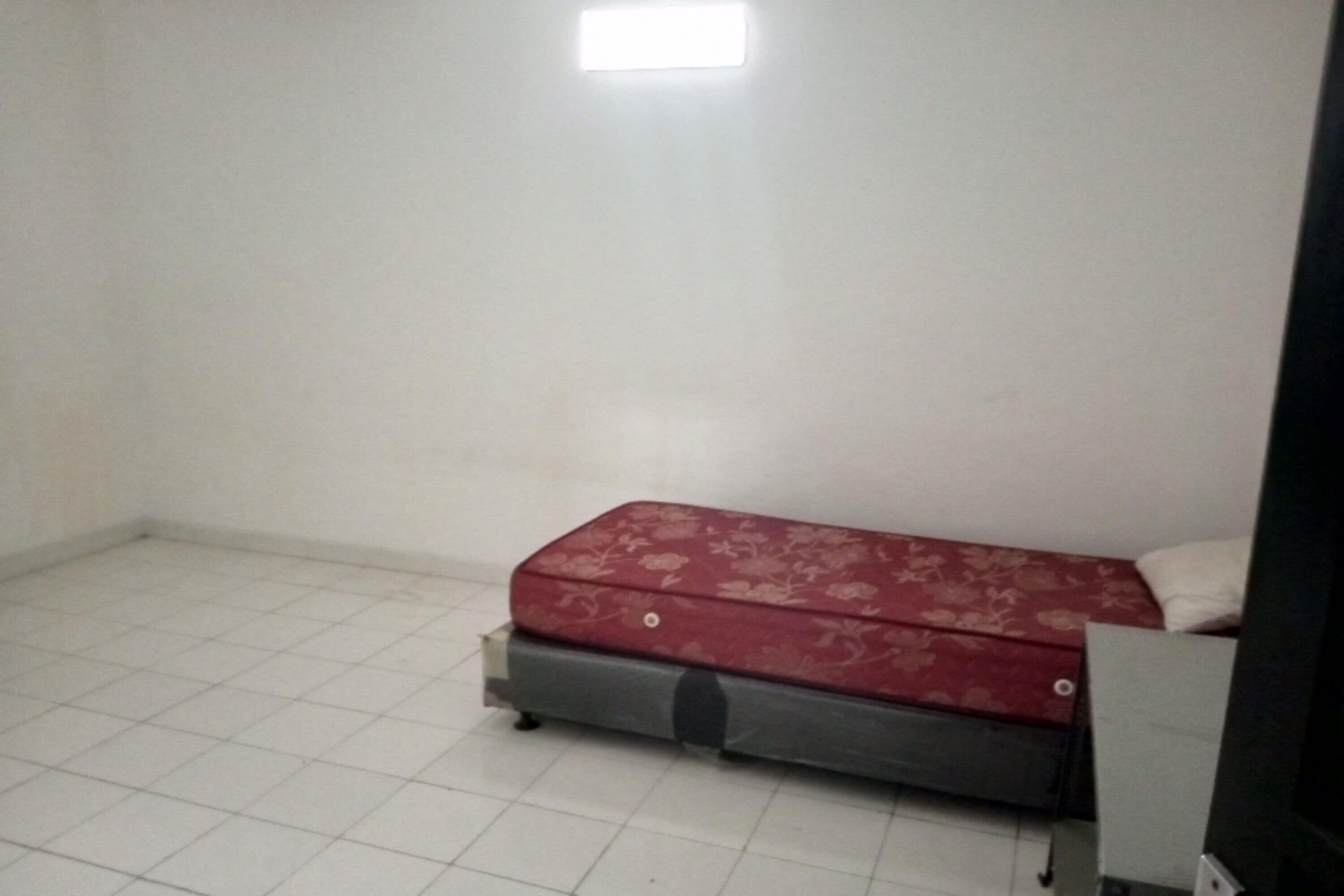 Une petite pièce avec un lit simple, une valise et un téléviseur.