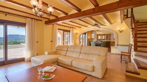 A spacious living area with a wooden ceiling, a beige sectional sofa, a wooden dining table with a bowl of fruit, and a view of the outdoors through large windows. - Wonderful and comfortable villa in Javea, Costa Blanca, Spain  with private pool for 4 persons (Javea)