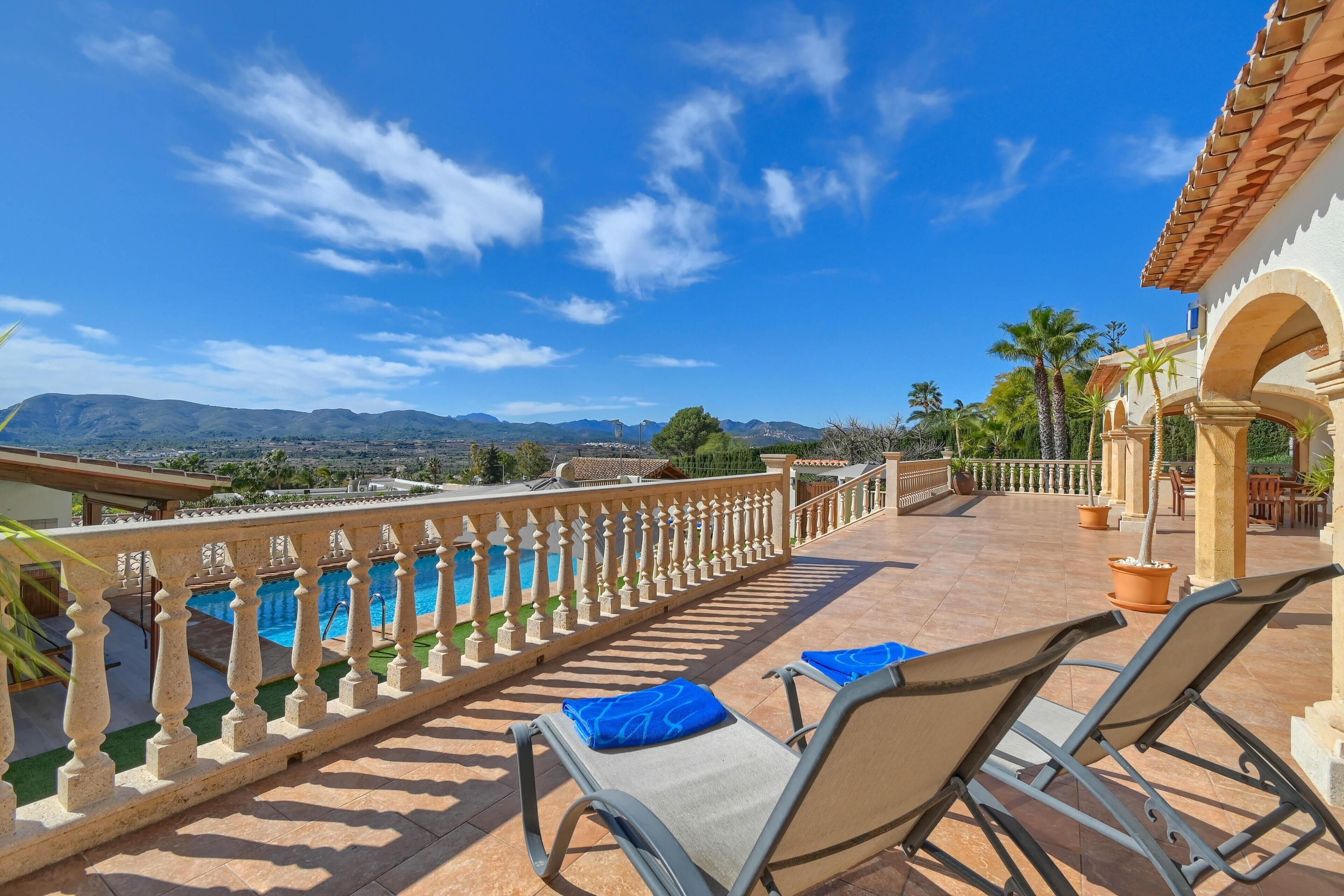 A terrace with a pool, lounge chairs, and a view of mountains.
