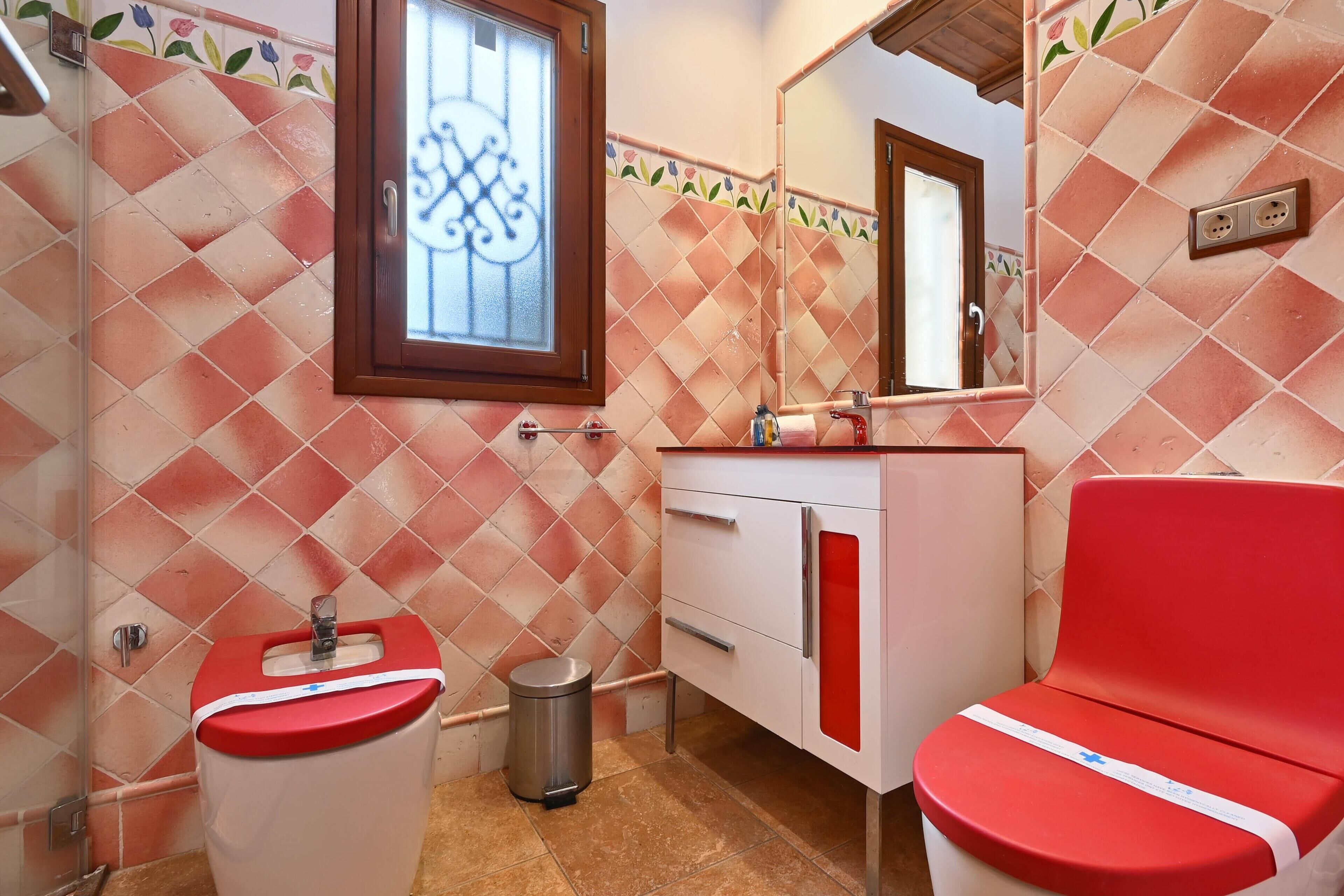 A bathroom with a red and white sink, a red toilet, a mirror, and a tiled wall with a floral pattern.
