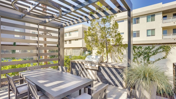 An outdoor patio with a wooden table and chairs, a grill, and a pergola. - Convenient Anaheim Condo: Walk to Angel Stadium (Anaheim)