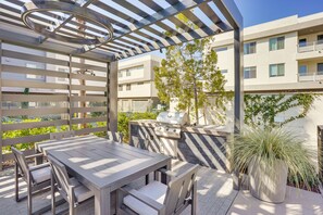 Un patio al aire libre con mesa y sillas de madera, una parrilla y una pérgola.