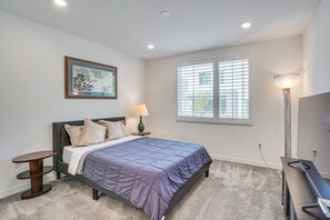 Un dormitorio con cama, mesita de noche, lámpara y un cuadro en la pared.