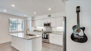 A modern kitchen with white cabinetry, a granite countertop island, stainless steel appliances, and a guitar on the wall. - Convenient Anaheim Condo: Walk to Angel Stadium (Anaheim)