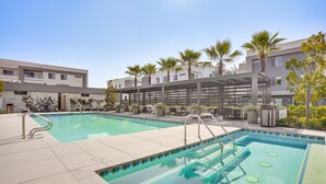 A swimming pool with clear blue water, surrounded by palm trees and modern buildings. - Convenient Anaheim Condo: Walk to Angel Stadium (Anaheim)