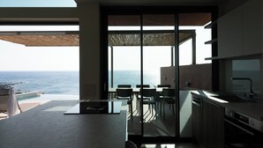 A modern kitchen with a view of the ocean, a dining area with chairs, and a large sliding glass door. - Casa Tarrha - Beachside Retreat with Private Heated Pool (Chania Town  Livadia)
