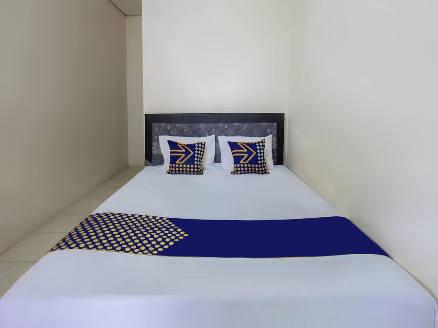 Una cama individual con cabecera oscura, dos almohadas con diseño geométrico y una colcha azul con estampado de lunares.
