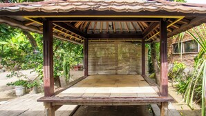 A wooden gazebo with a sloped roof, surrounded by greenery and a brick wall. - SPOT ON 93724 Songgong Homestay (Mertak)