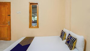 A bedroom with a wooden door, a small window, a bed with white bedding and patterned pillows, and a blue and yellow bedspread. - SPOT ON 93724 Songgong Homestay (Mertak)