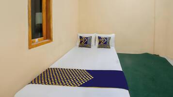 Una cama individual con colchón blanco, dos almohadas con diseño geométrico, una colcha azul y amarilla, y una alfombra verde.