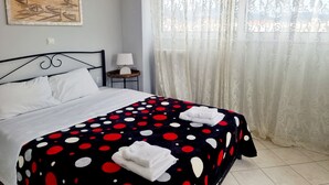 Una cama bien hecha con sábanas blancas, una colcha de lunares y dos toallas dobladas. Se ve una mesita de noche con una lámpara y una obra de arte enmarcada.