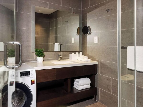A modern bathroom with a large mirror, a washing machine, and a dark wooden vanity. - Citadines Nanhai Foshan (Foshan)
