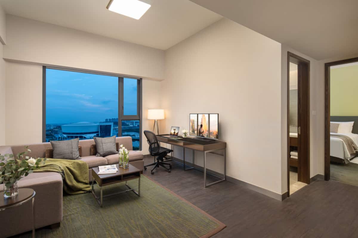 A modern hotel room with a large window, a desk, a comfortable sofa, and a bed.