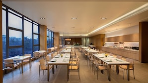 A spacious dining area with multiple tables and chairs, large windows offering views of the city, and a modern kitchen area with a counter and appliances. - Citadines Nanhai Foshan (Foshan)