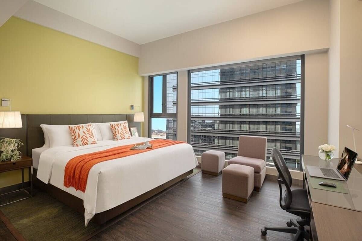 A hotel room with a bed, a desk, a chair, and large windows.