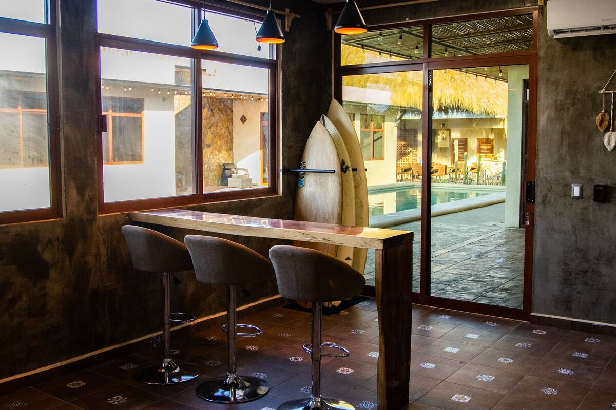 A bar area with a wooden table and bar stools, large windows, and a ceiling fan.