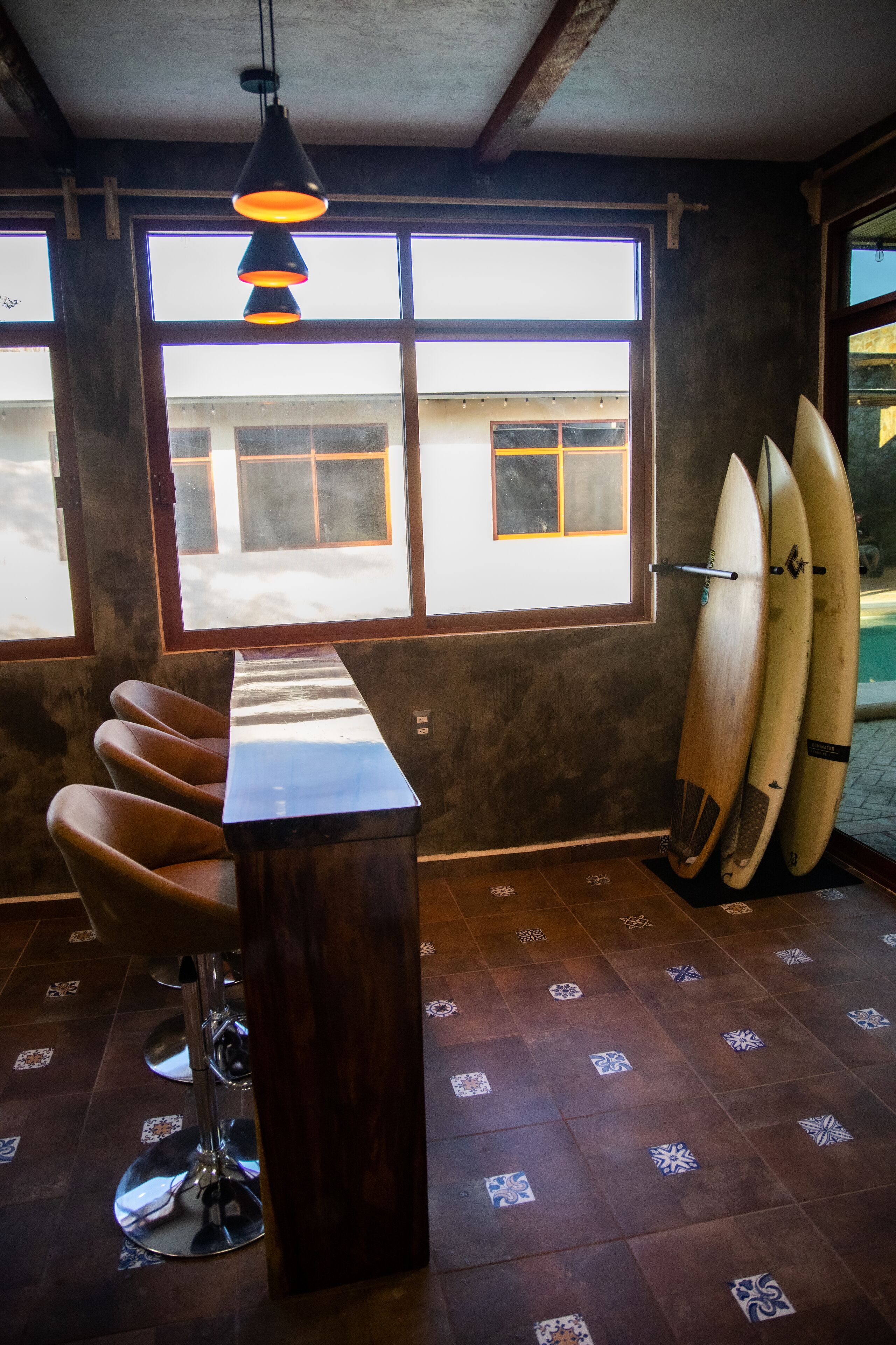 A bar area with a long wooden counter, bar stools, and surfboards against the wall.