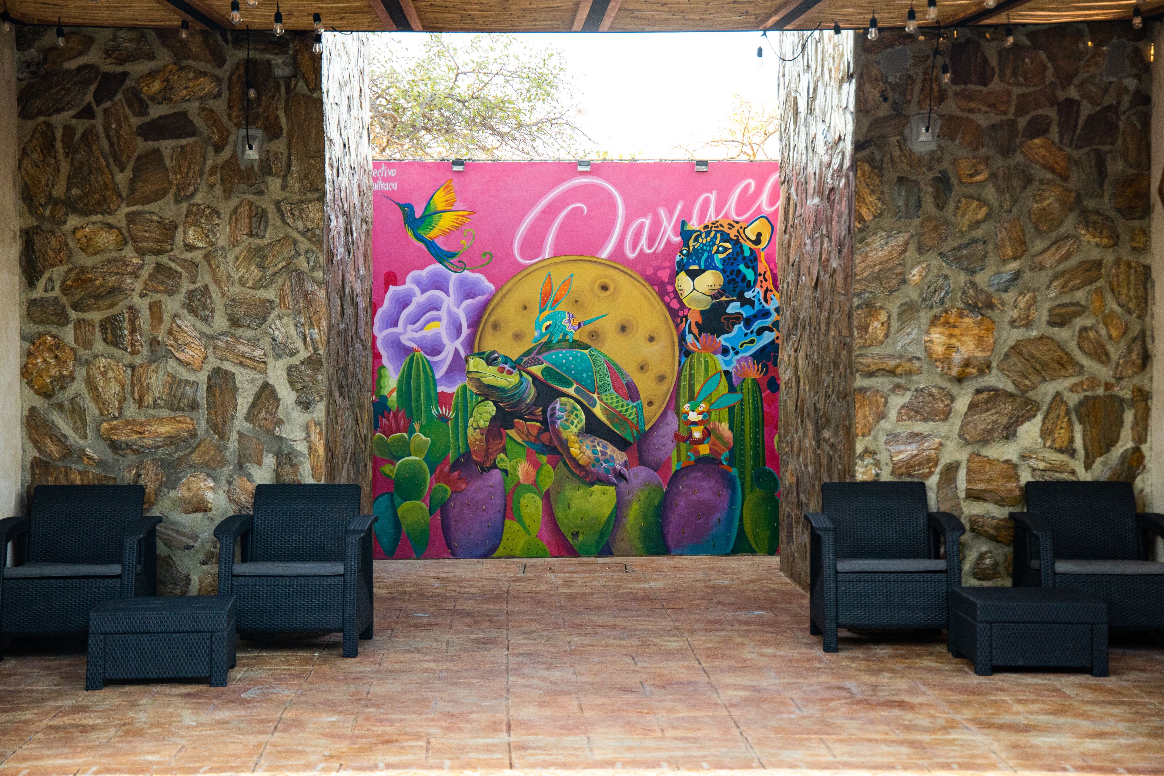 A stone-walled room with a colorful mural, two wicker chairs, and a tiled floor.