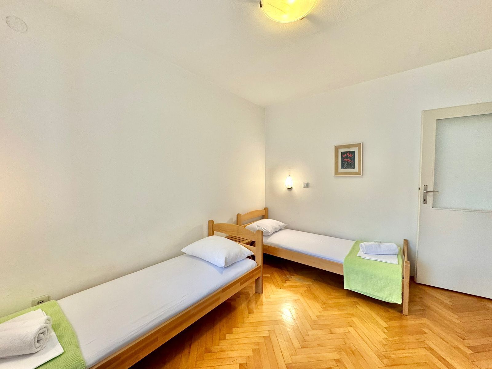 A small, clean room with two wooden beds, a green towel, and a door.